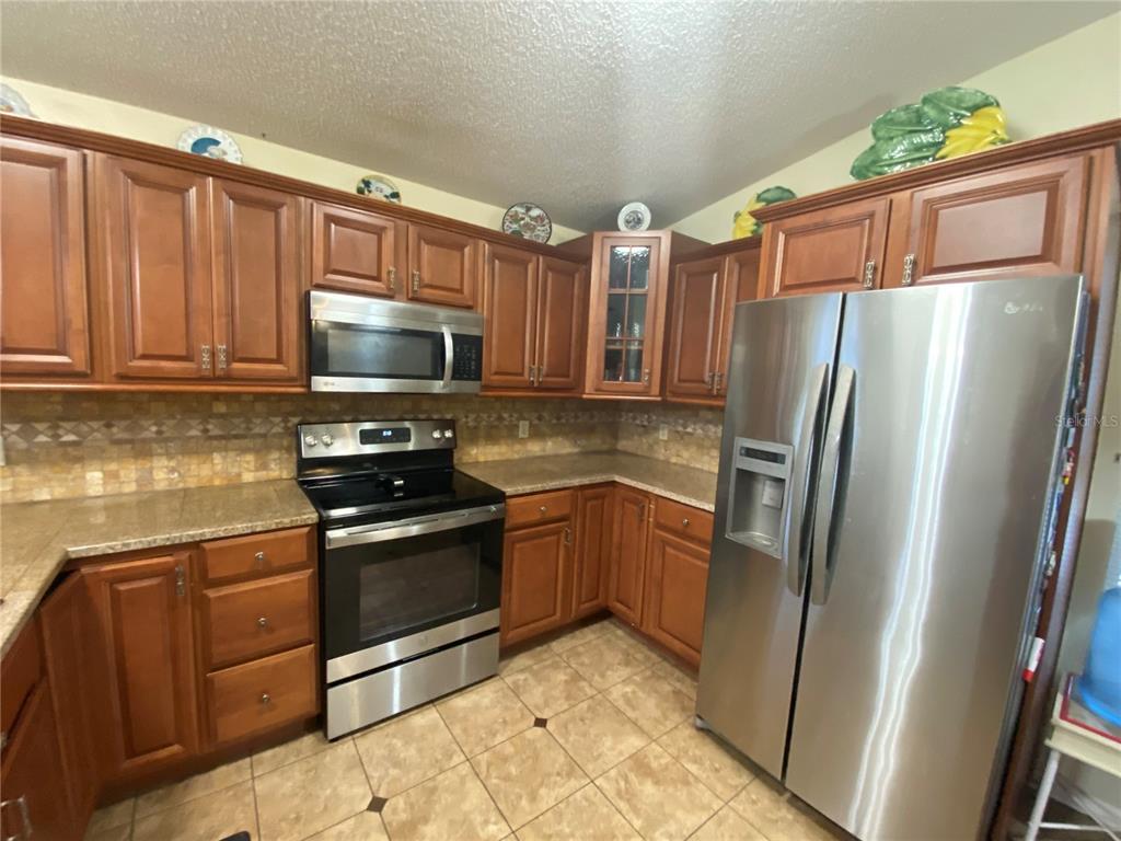A kitchen features wood cabinets, stainless steel appliances, granite countertops, and tiled flooring — 1420 WINDJAMMER PLACE, VALRICO, FL