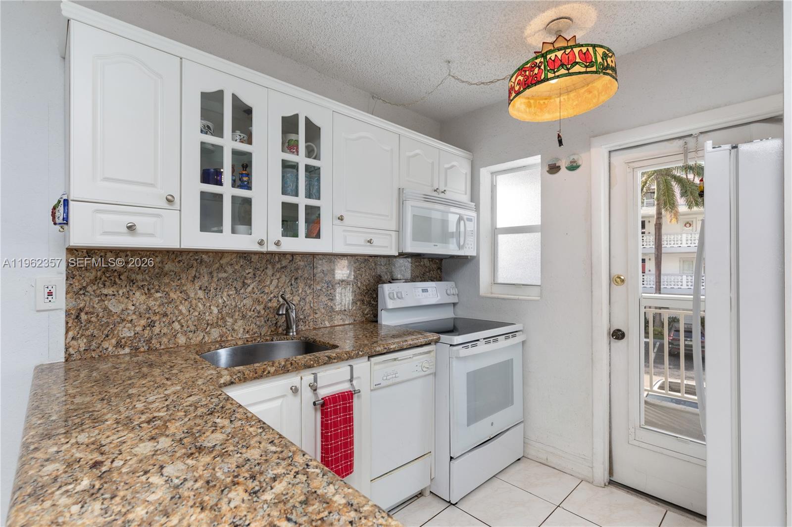 A kitchen features white cabinetry, granite countertops, white appliances, and a stained-glass pendant light — 3127 S Ocean Dr # 219, Hallandale Beach FL 33009, HALLANDALE BEACH, FL