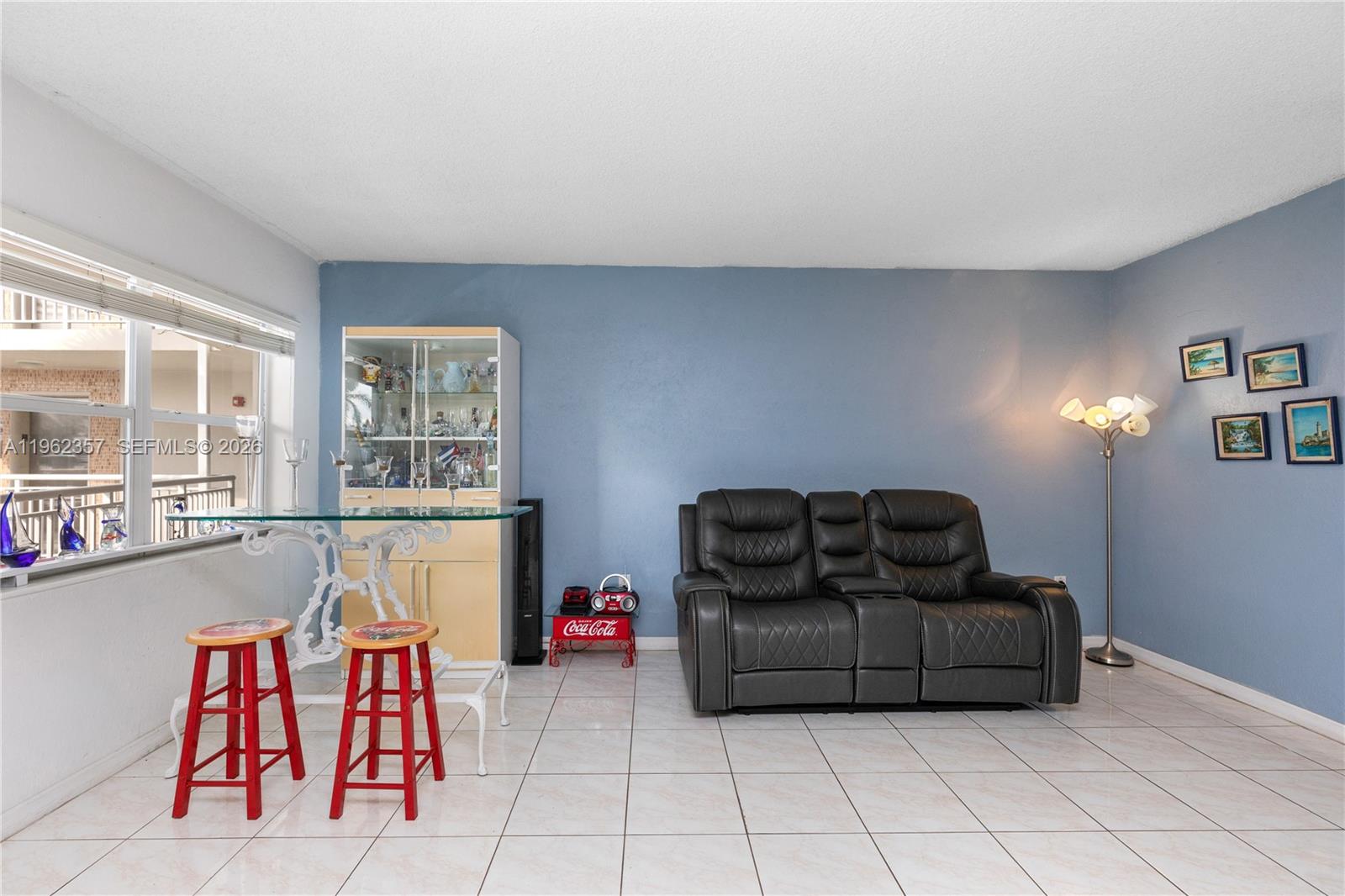 A living room features a dark leather loveseat, a glass-topped table with red stools, and tile flooring — 3127 S Ocean Dr # 219, Hallandale Beach FL 33009, HALLANDALE BEACH, FL