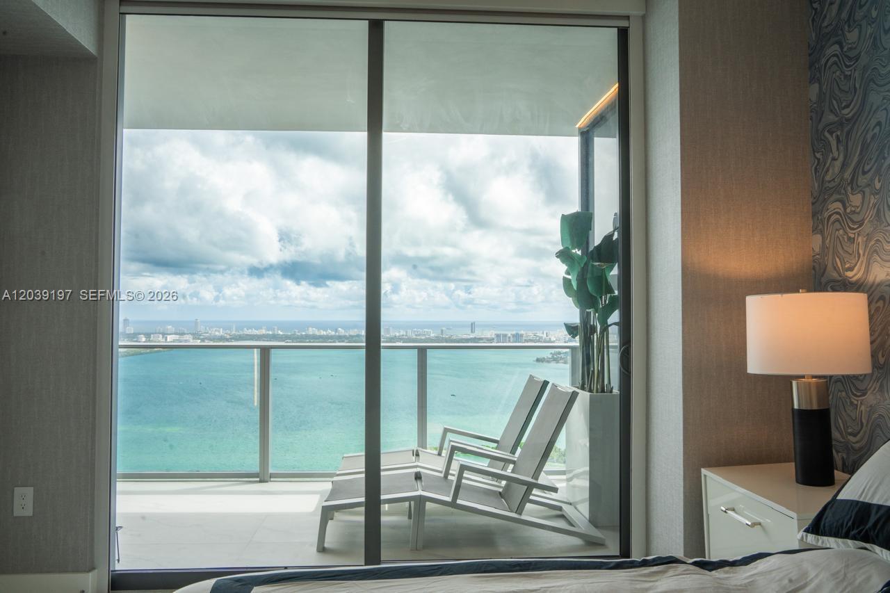 A bedroom features a sliding glass door opening to a balcony with lounge chairs and water — 711 NE 23rd Ter # 5304B, Miami FL 33137, MIAMI, FL