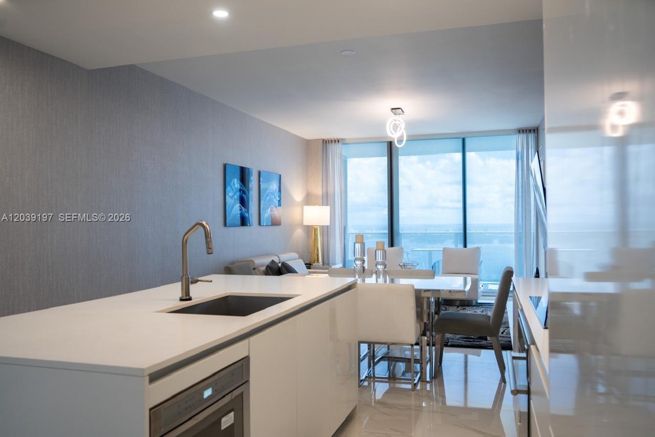 A modern kitchen island with a sink overlooks a dining area and floor-to-ceiling windows — 711 NE 23rd Ter # 5304B, Miami FL 33137, MIAMI, FL