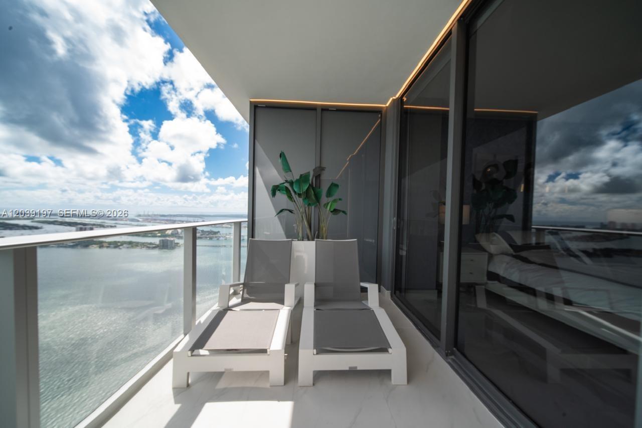 A high-rise balcony features two lounge chairs, a potted plant, and a water view — 711 NE 23rd Ter # 5304B, Miami FL 33137, MIAMI, FL