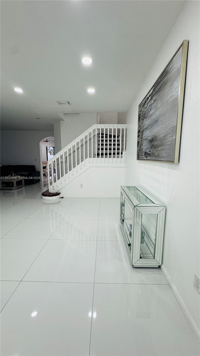 A bright, tiled entryway features a white staircase, a mirrored console table, and wall art — 3355 W 90th Ter, Hialeah FL 33018, HIALEAH, FL