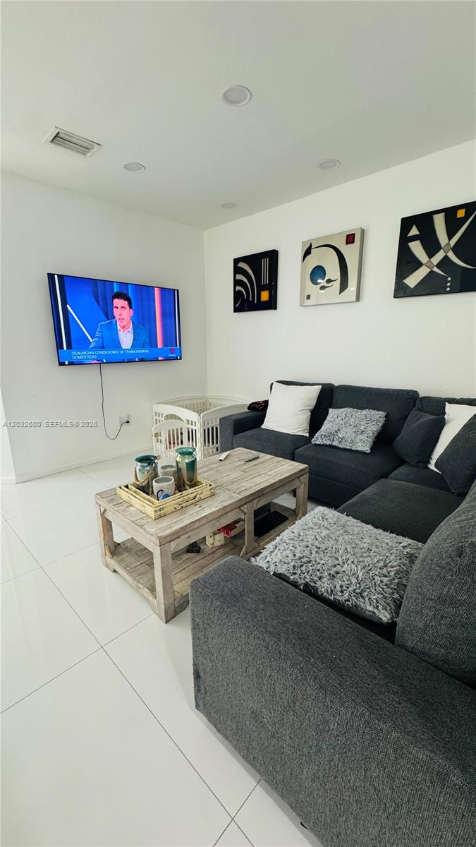A living room features a dark sectional sofa, a rustic wooden coffee table, and a wall-mounted television — 3355 W 90th Ter, Hialeah FL 33018, HIALEAH, FL