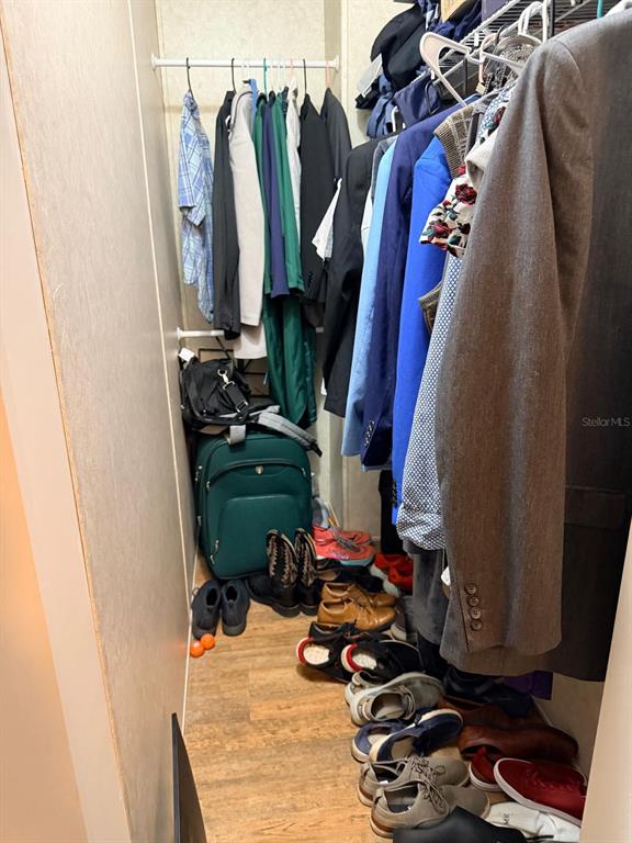 A narrow walk-in closet contains hanging clothes, a green suitcase, and shoes on the floor — 3520 E GASKINS ROAD Lot 5, BARTOW, FL