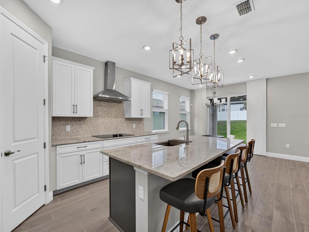 A modern kitchen features white cabinets, granite countertops, a dark island, and pendant lighting — 2292 BEAR PEAK RD. ROAD, MINNEOLA, FL