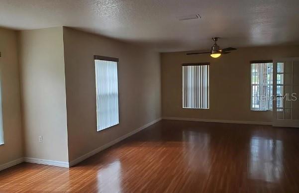An empty living room features wood-look flooring, a ceiling fan, and vertical blinds on windows — 815 W REMBRANDT WAY UNIT 424, INVERNESS, FL