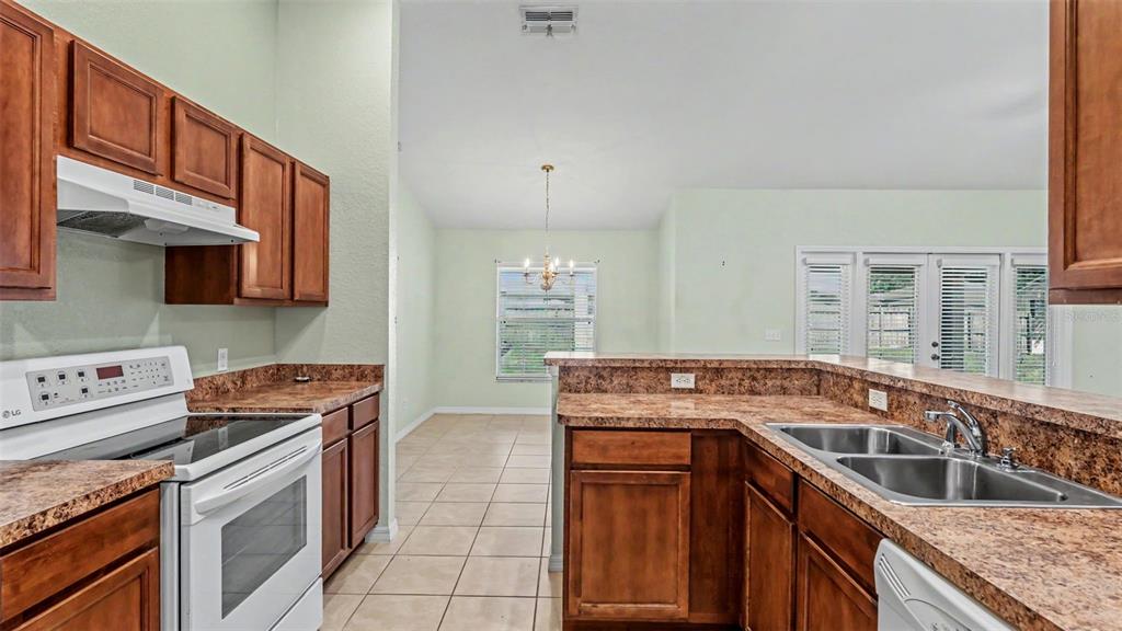 A kitchen with wood cabinets, laminate countertops, and white appliances overlooks a dining area — 265 MAJESTIC GARDENS LANE, WINTER HAVEN, FL