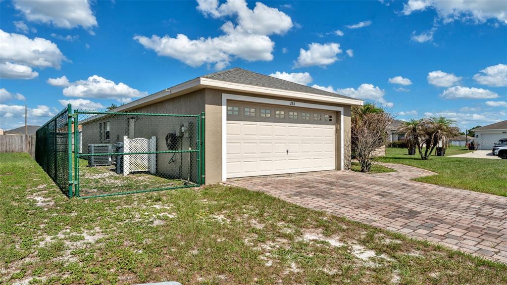 A detached garage with a paver driveway and a fenced side yard under a blue sky — 265 MAJESTIC GARDENS LANE, WINTER HAVEN, FL