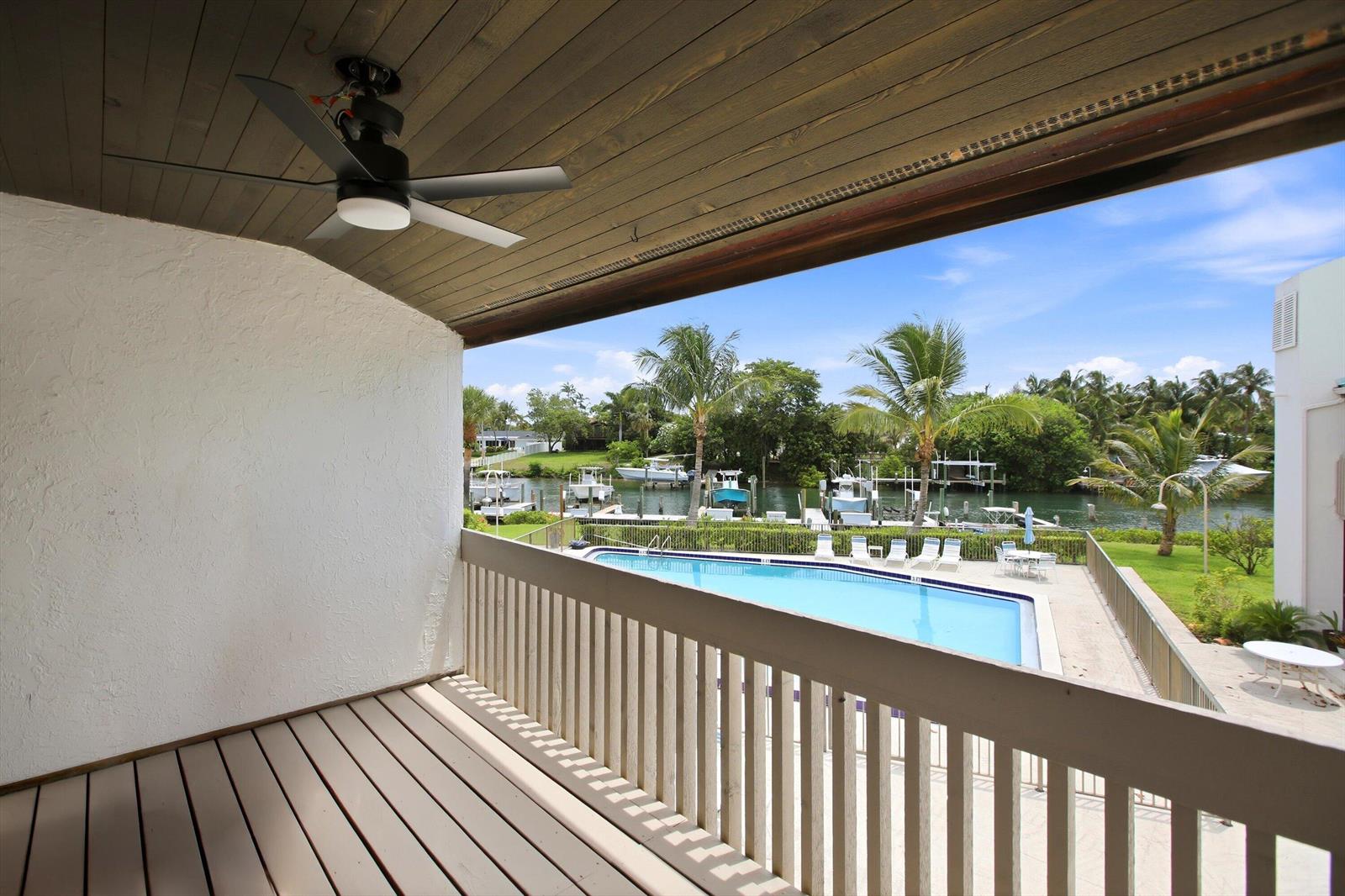 A balcony with a ceiling fan overlooks a swimming pool and a canal with boats — 412 Southwind Drive # E2, North Palm Beach FL 33408, NORTH PALM BEACH, FL