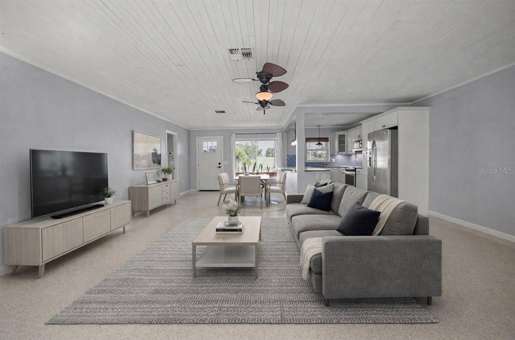 An open-concept living and dining area features a gray sofa, wood furniture, and white ceilings — 951 GREENWAY AVENUE, DUNEDIN, FL