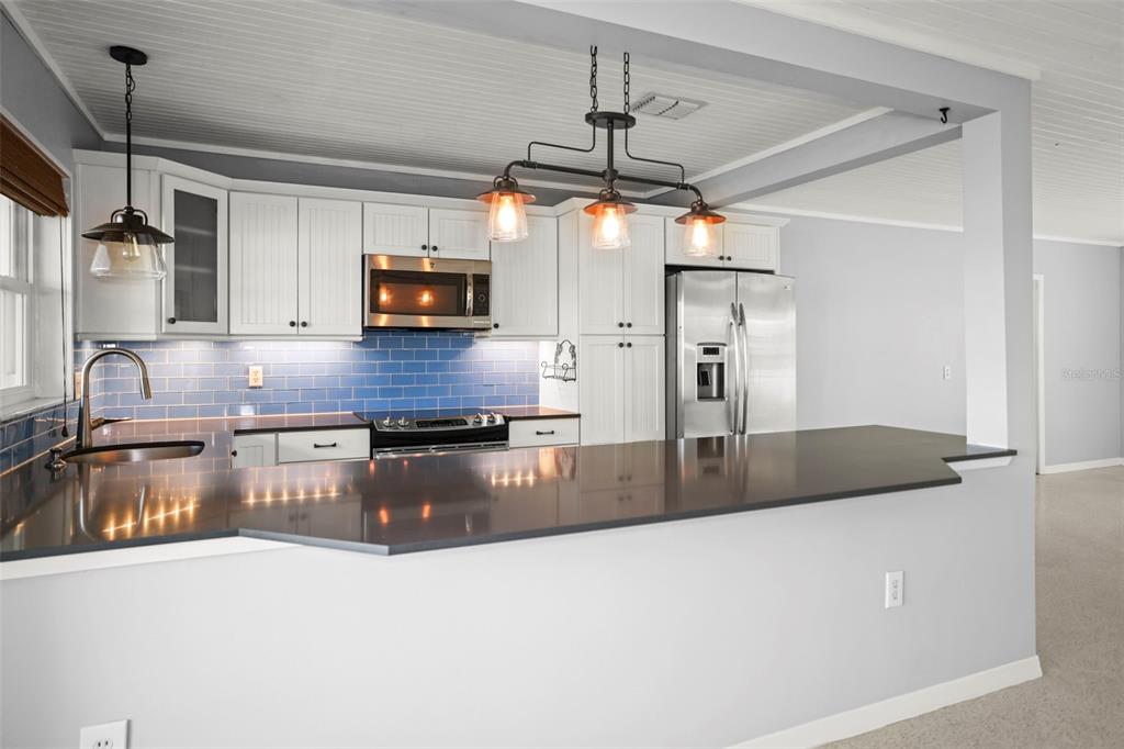 A kitchen with white cabinets, blue subway tile backsplash, and a dark countertop peninsula — 951 GREENWAY AVENUE, DUNEDIN, FL