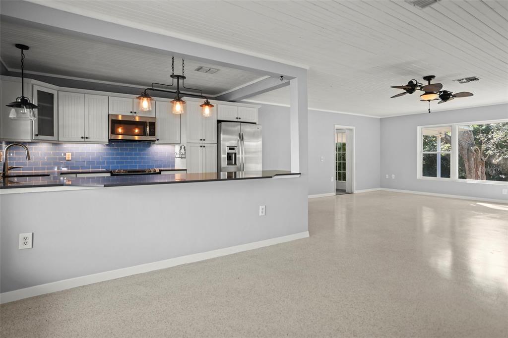 A kitchen with white cabinets and blue tile backsplash overlooks a spacious, light-filled living area — 951 GREENWAY AVENUE, DUNEDIN, FL