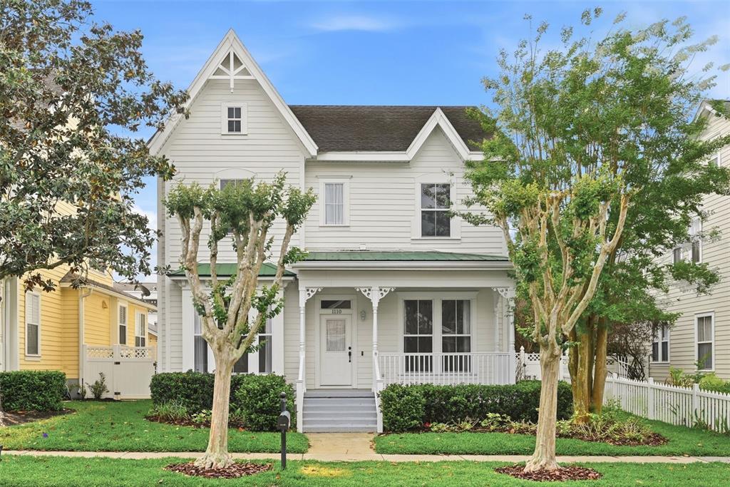 A two-story white house with a front porch, green metal roof, and two small trees — 1110 RUSH COURT, CELEBRATION, FL