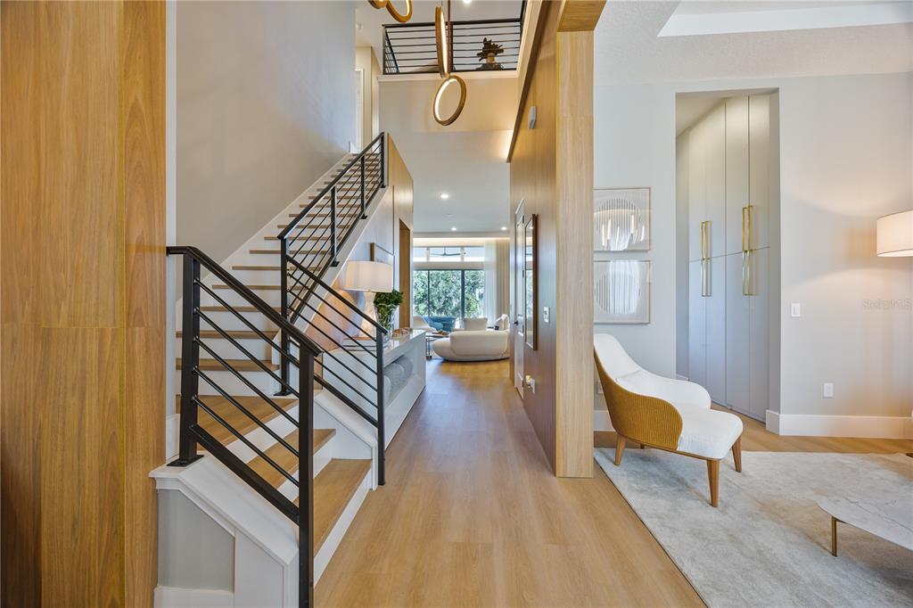 A modern entryway features a wooden staircase with black railings, light flooring, and a lounge area — 16077 BARKLY RIDGE COURT, WINTER GARDEN, FL