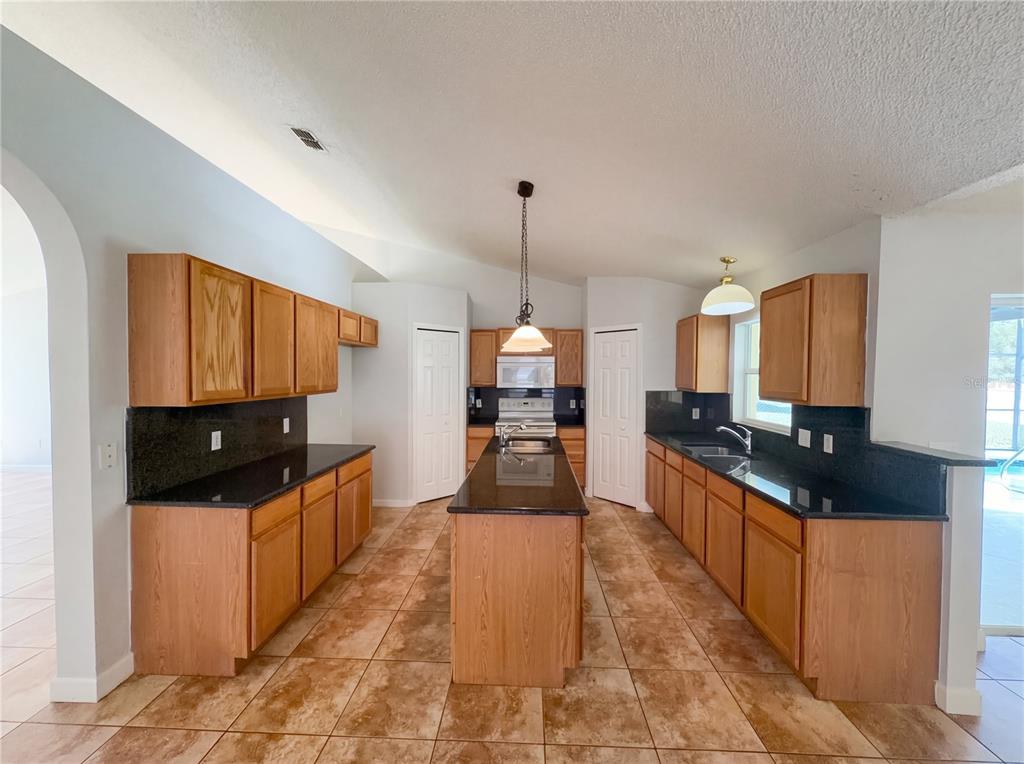 A kitchen with wood cabinets, black countertops, a central island, and tiled flooring — 107 HERRING WAY, KISSIMMEE, FL