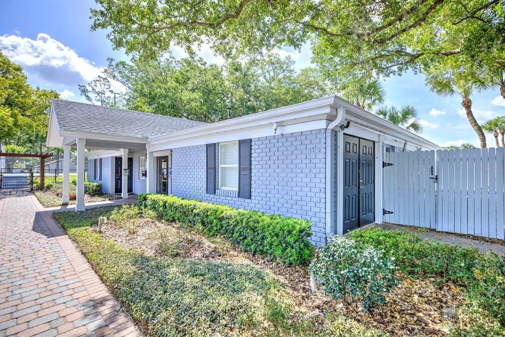 A single-story gray brick building features a covered walkway, dark shutters, and a white fence — 262 LEWFIELD CIRCLE UNIT 262, WINTER PARK, FL