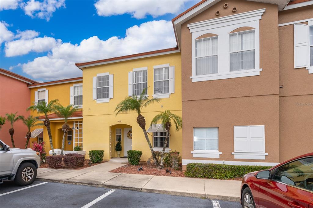 A yellow and brown multi-story townhouse exterior with palm trees and parked cars in front — 979 PARK TERRACE CIRCLE, KISSIMMEE, FL