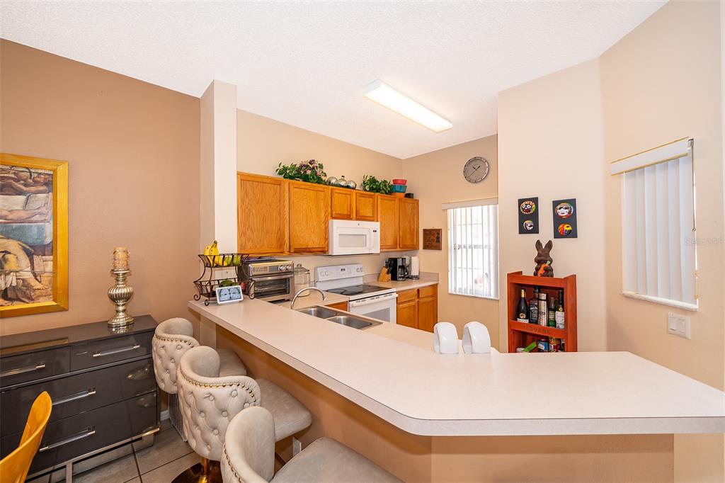 A kitchen with light-colored countertops, wooden cabinets, and a breakfast bar with three stools — 979 PARK TERRACE CIRCLE, KISSIMMEE, FL