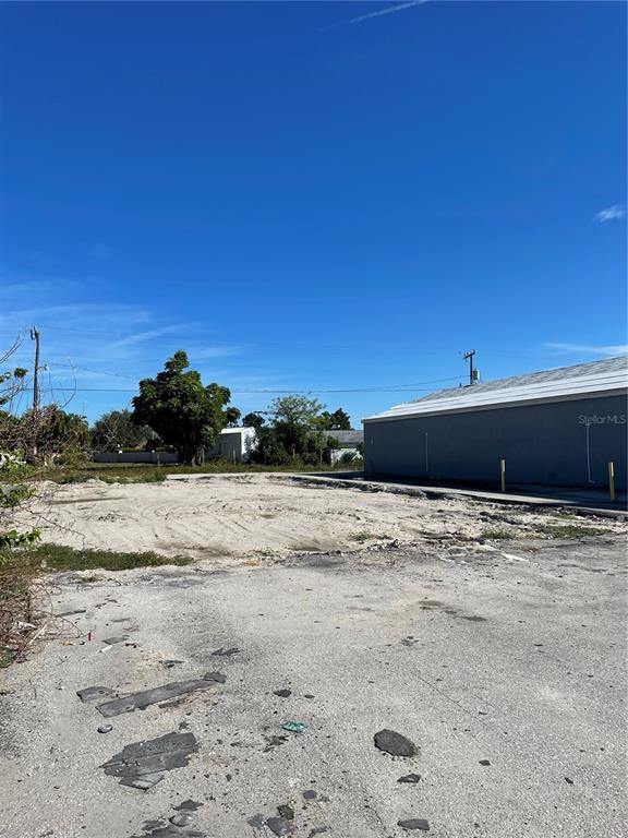 A vacant, sandy lot sits adjacent to a grey building under a clear blue sky — 3782 TAMIAMI TRAIL UNIT B, PORT CHARLOTTE, FL