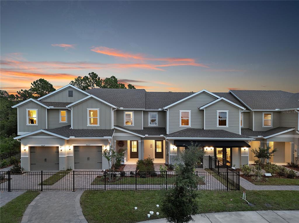 A multi-unit townhouse exterior features gray siding, multiple gabled roofs, and a black metal fence — 16639 LUMINARY, CLERMONT, FL