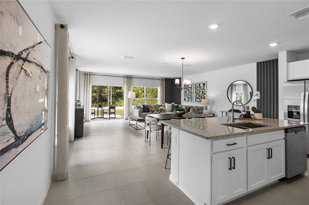 A bright open-concept kitchen and living area features white cabinets, granite countertops, and tile flooring — 16639 LUMINARY, CLERMONT, FL