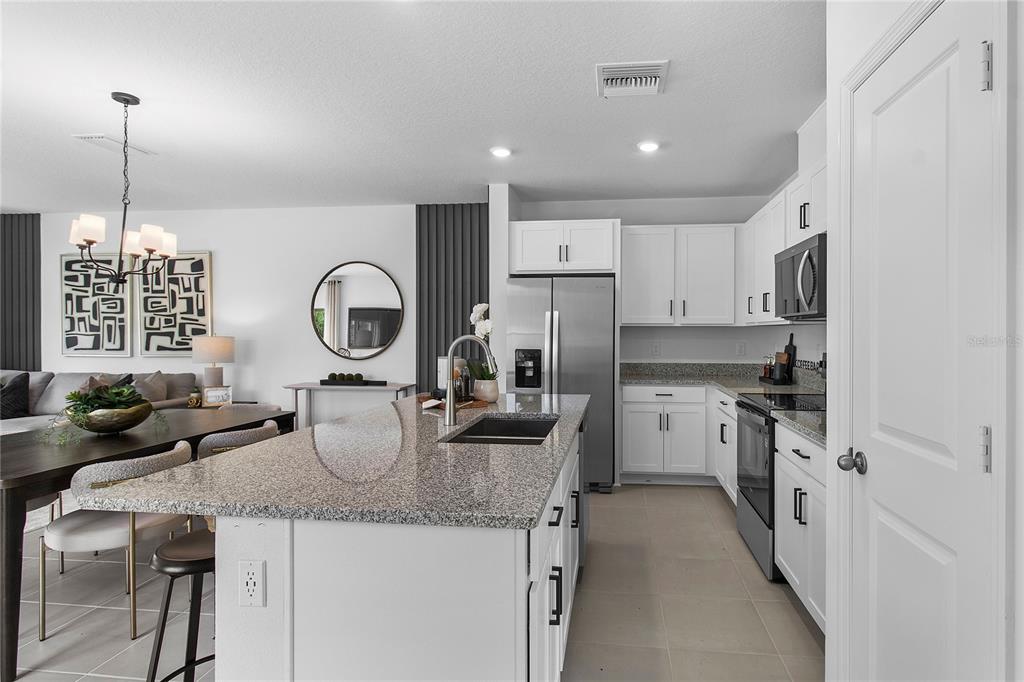 A modern kitchen features white cabinets, granite countertops, a central island, and stainless steel appliances — 16639 LUMINARY, CLERMONT, FL