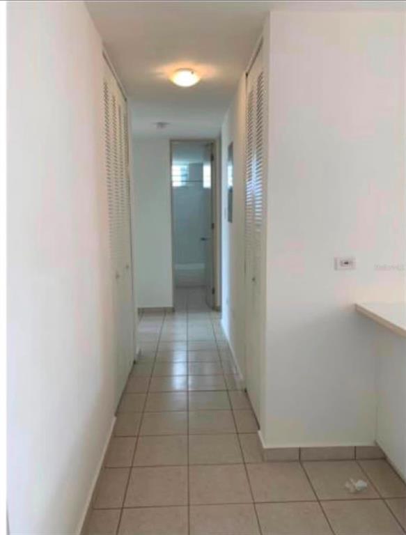 A narrow hallway with light-colored tile flooring leads to a bathroom with louvered closet doors — Apartments MONTESOL UNIT E-312, FAJARDO, PR