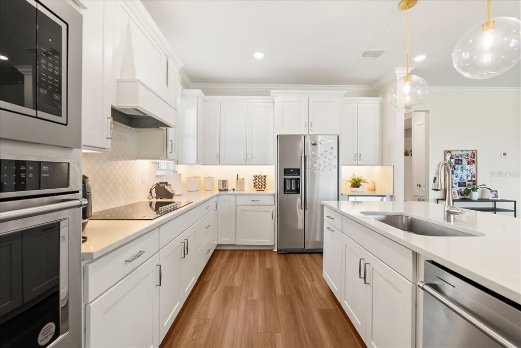 A modern white kitchen features stainless steel appliances, quartz countertops, and light wood-look flooring — 3208 SAILING PIER AVENUE, WINTER GARDEN, FL