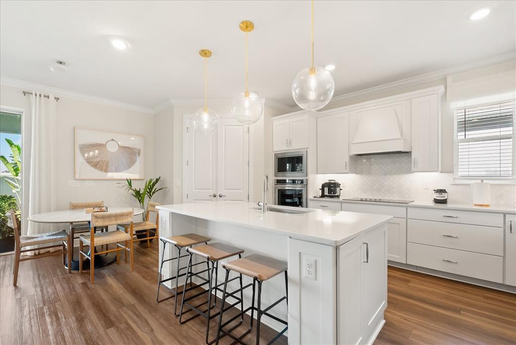 A modern kitchen features white cabinetry, a central island with bar stools, and dining area — 3208 SAILING PIER AVENUE, WINTER GARDEN, FL