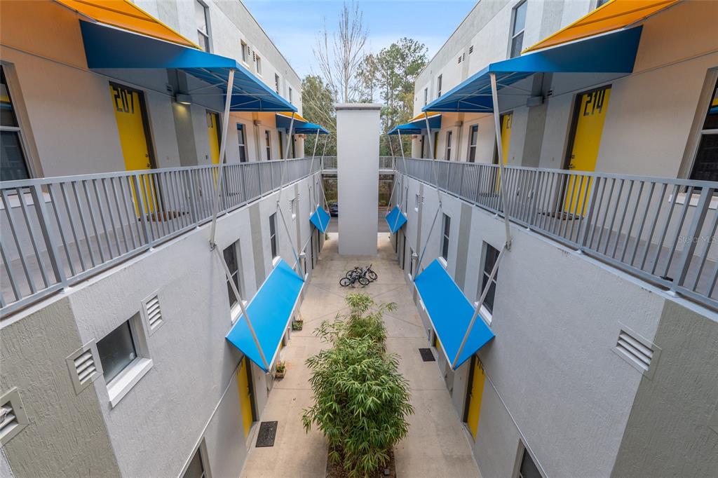 An outdoor courtyard between two apartment buildings features yellow doors, blue awnings, and bicycles — 2515 SW 35TH PLACE UNIT 219, GAINESVILLE, FL