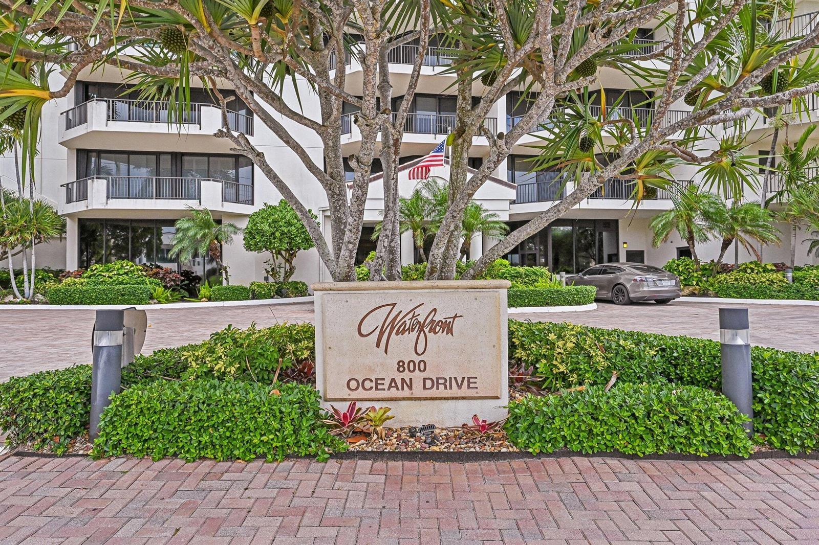 A stone sign stands in front of a multi-story building with balconies and palm trees — 800 Ocean Drive # 1105, Juno Beach FL 33408, JUNO BEACH, FL