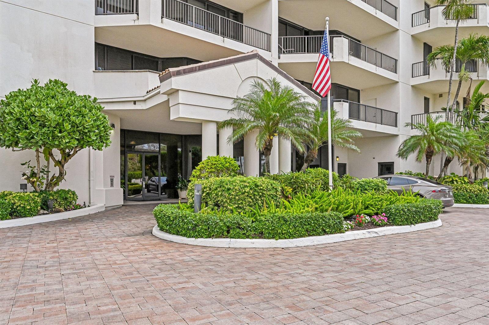 The exterior of a multi-story building features a paved driveway, landscaping, and an American flag — 800 Ocean Drive # 1105, Juno Beach FL 33408, JUNO BEACH, FL
