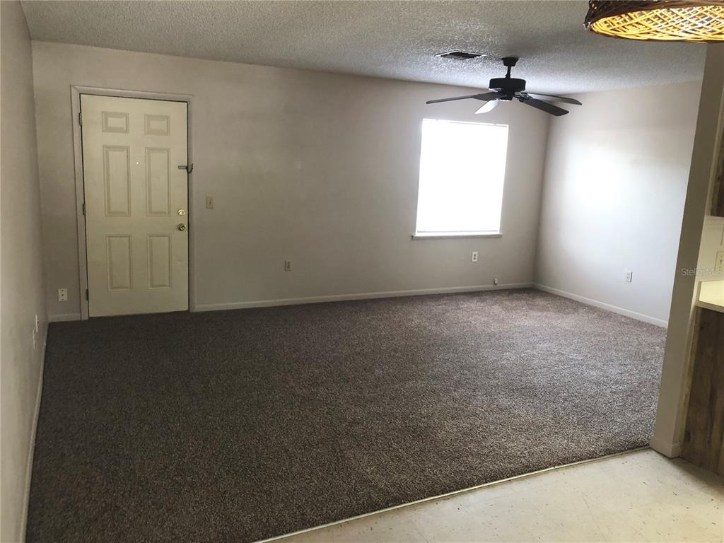 A living room with beige carpet, a ceiling fan, a window, and an entry door — 308 W CRESCENT DRIVE UNIT 2, LAKELAND, FL