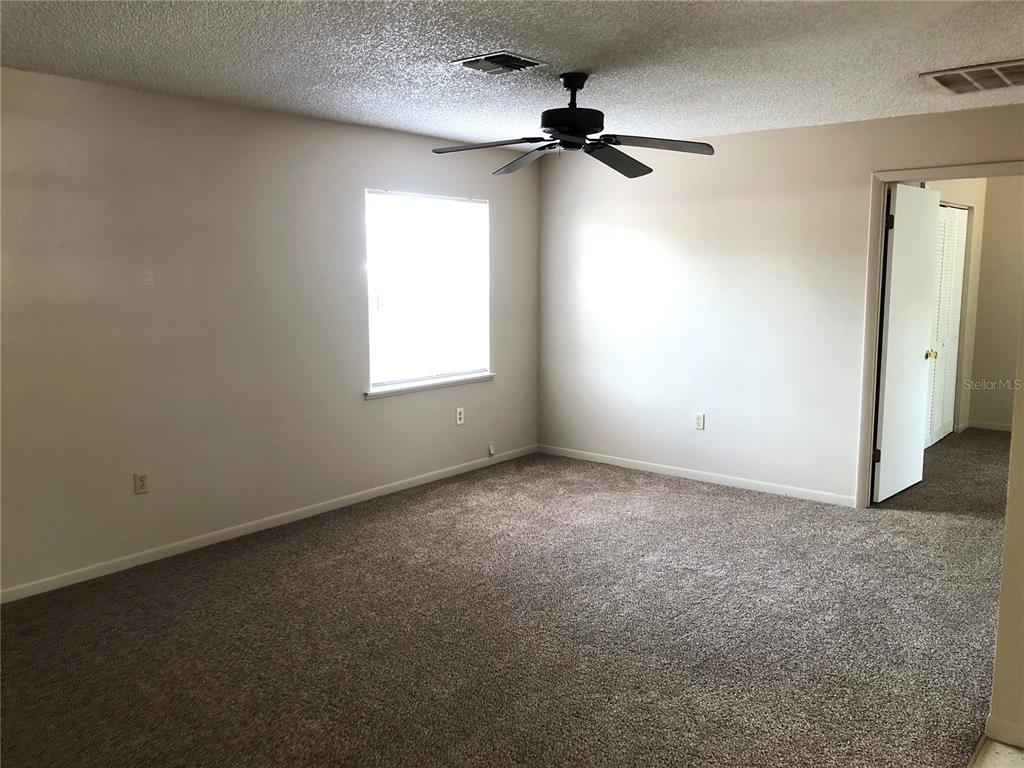 An empty bedroom features beige walls, brown carpeting, a ceiling fan, and a window — 308 W CRESCENT DRIVE UNIT 2, LAKELAND, FL