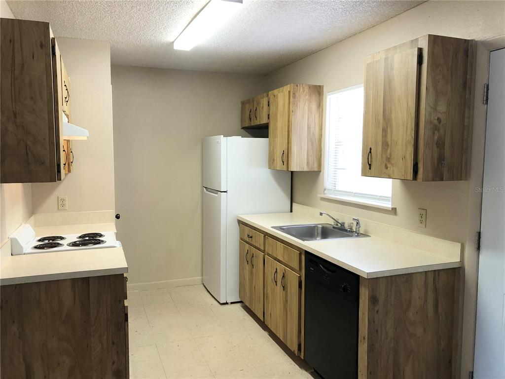A kitchen features wood-grain cabinets, white countertops, a white refrigerator, and a black dishwasher — 308 W CRESCENT DRIVE UNIT 2, LAKELAND, FL