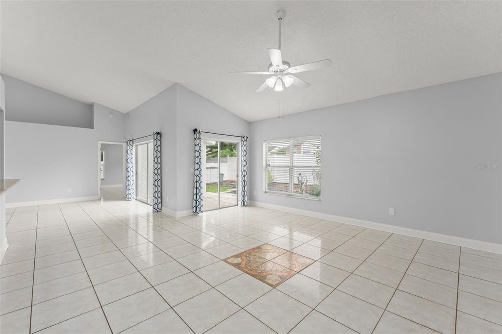 A bright living room features light-colored tile flooring, a vaulted ceiling, and sliding glass doors — 632 HERONS NEST COURT, ORLANDO, FL