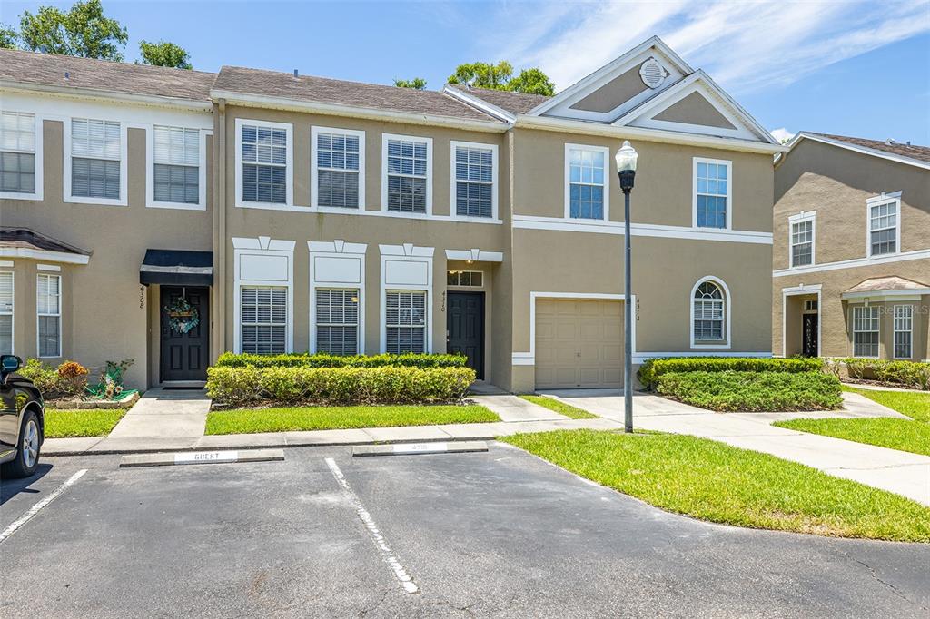 A two-story townhouse with tan stucco siding, a garage, and guest parking spaces in front — 4310 FINCASTLE COURT, TAMPA, FL