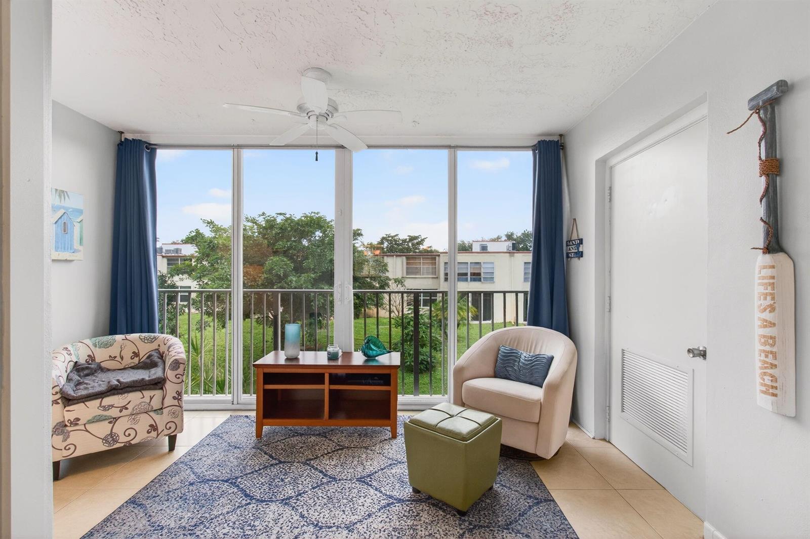 A sunroom features a patterned rug, two armchairs, a wooden coffee table, and floor-to-ceiling windows — 10 Willowbrook # 205, Delray Beach FL 33446, DELRAY BEACH, FL
