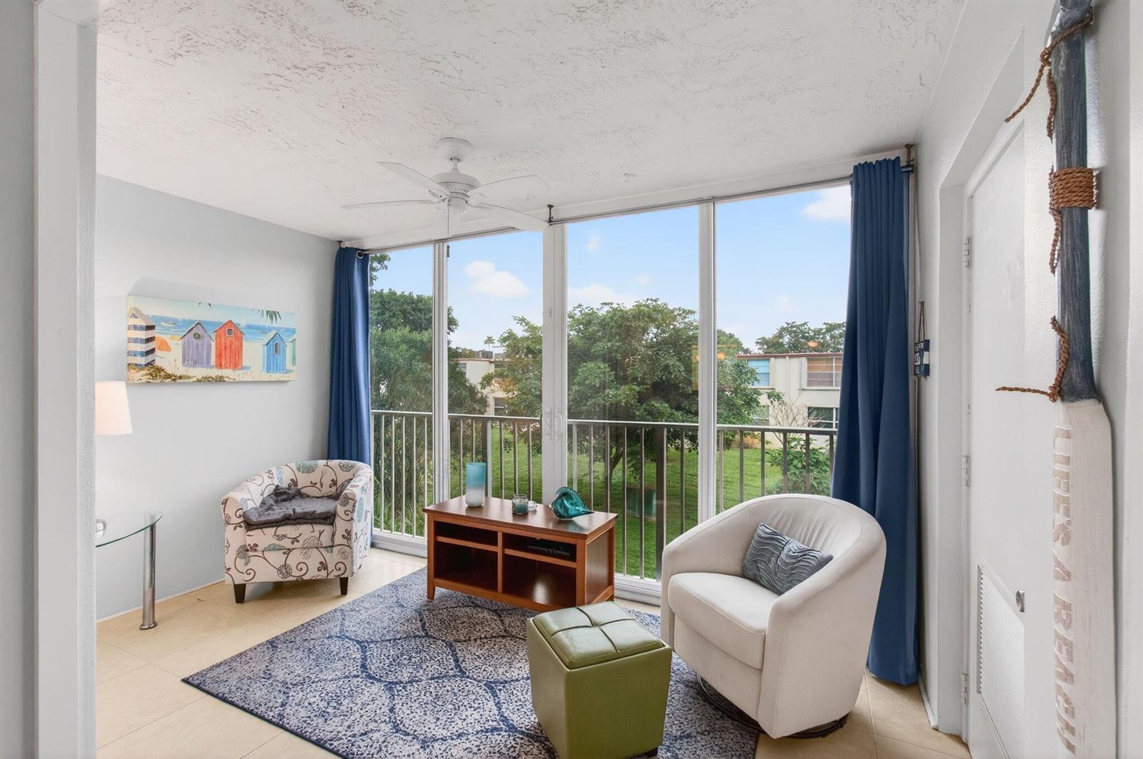 A sunroom features a patterned rug, two armchairs, a wooden console, and floor-to-ceiling windows — 10 Willowbrook # 205, Delray Beach FL 33446, DELRAY BEACH, FL