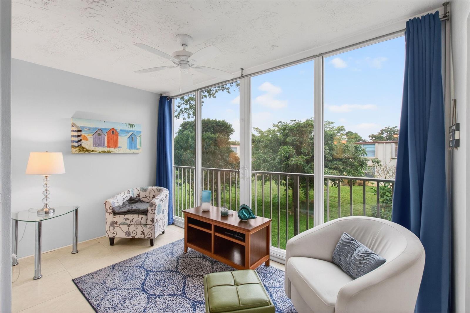 A sunroom features a patterned armchair, a white swivel chair, and large windows overlooking trees — 10 Willowbrook # 205, Delray Beach FL 33446, DELRAY BEACH, FL