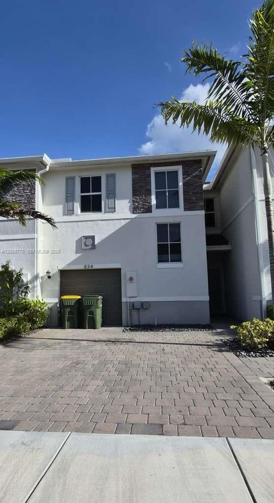 A two-story townhouse exterior features a paved driveway, a garage, and stone-accented siding — 834 SE 16th Ct, Homestead FL 33034, HOMESTEAD, FL