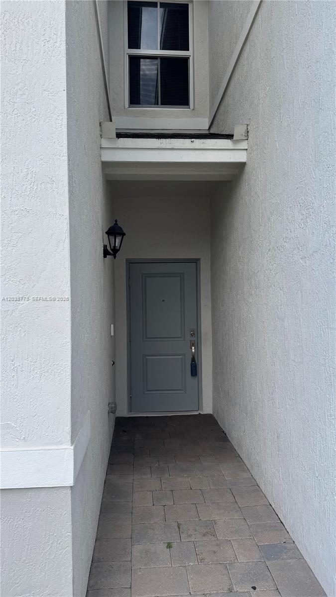 A gray front door is recessed in a narrow entryway with a paved floor — 834 SE 16th Ct, Homestead FL 33034, HOMESTEAD, FL