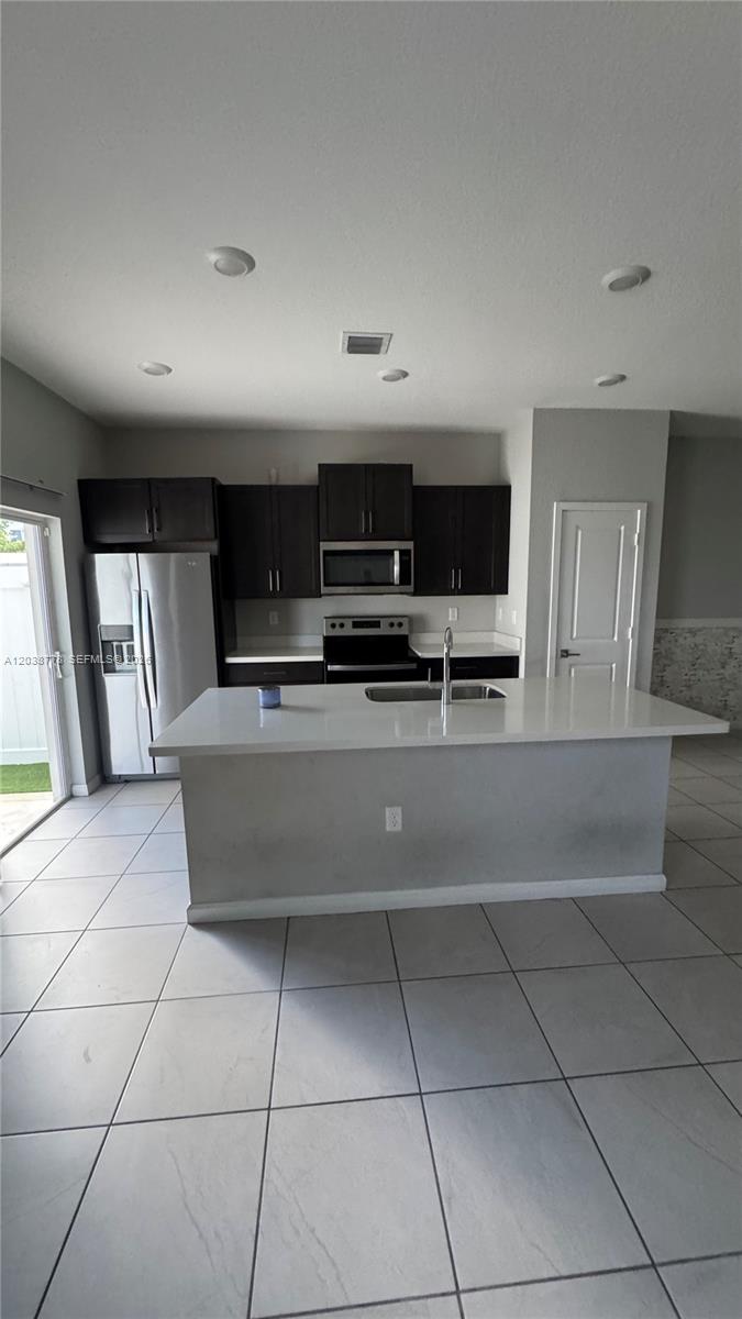 A kitchen features dark cabinets, stainless steel appliances, a white island, and light tile flooring — 834 SE 16th Ct, Homestead FL 33034, HOMESTEAD, FL