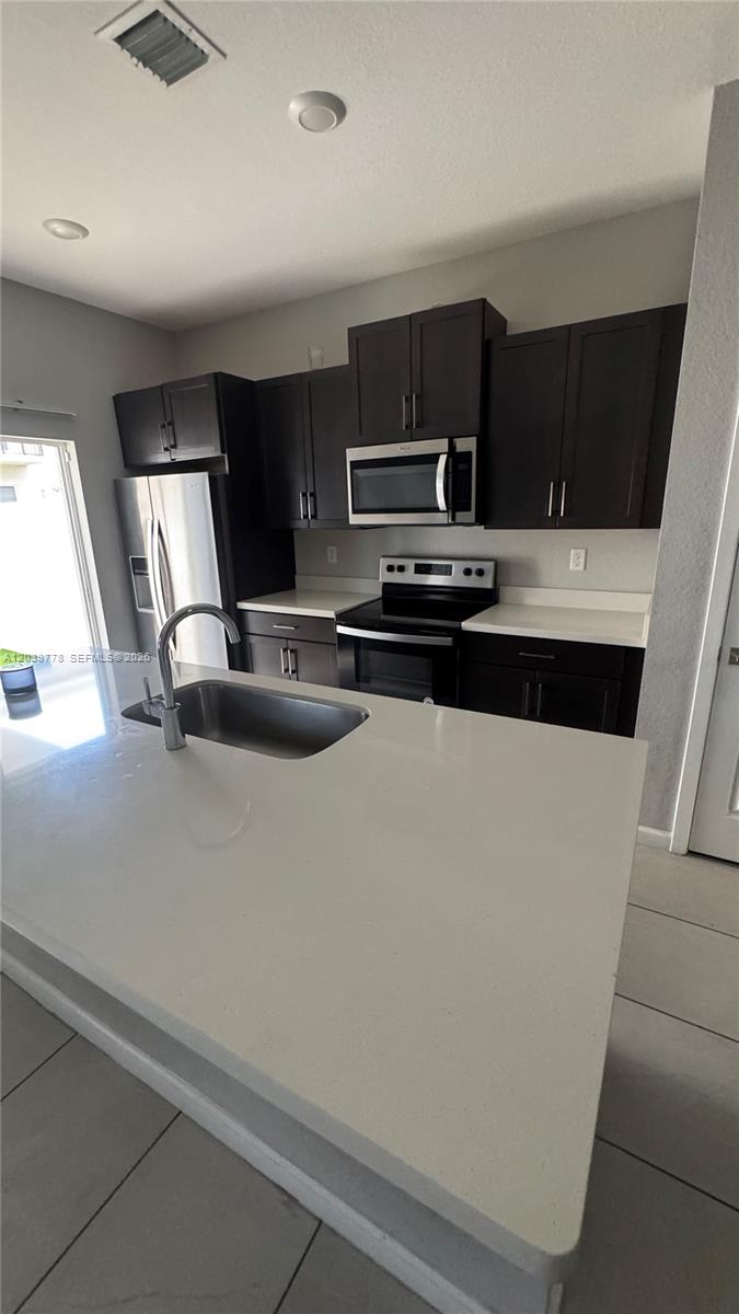 A kitchen features dark cabinetry, stainless steel appliances, and a large white quartz island — 834 SE 16th Ct, Homestead FL 33034, HOMESTEAD, FL