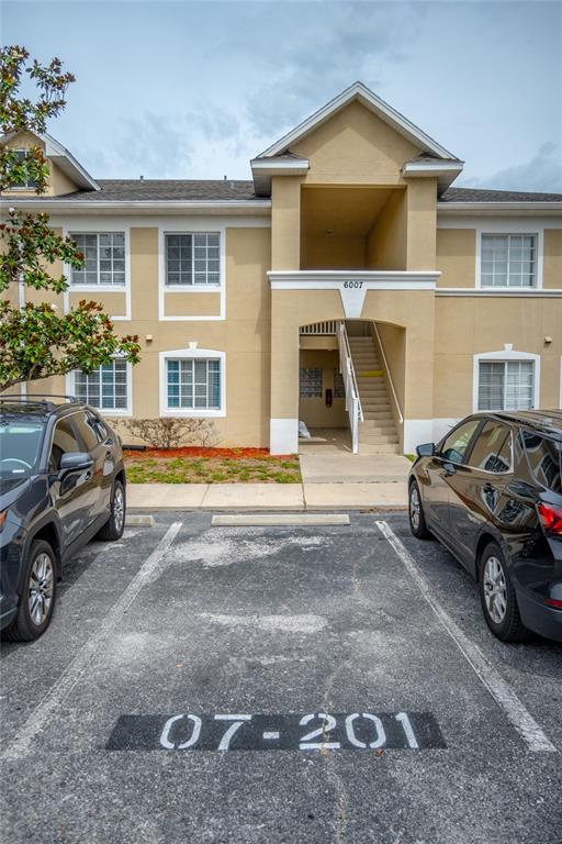 A two-story apartment building exterior features tan stucco walls, white trim, and a central staircase — 6007 SKYDALE WAY UNIT 201, RIVERVIEW, FL