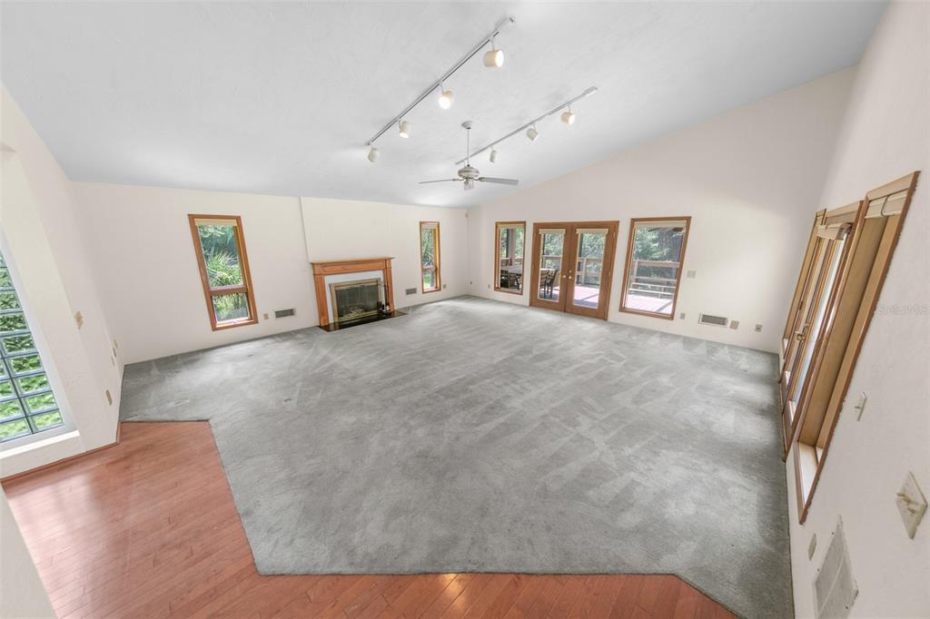A spacious living room features a vaulted ceiling, gray carpeting, wood flooring, and a fireplace — 59 BEACH STREET, PONCE INLET, FL