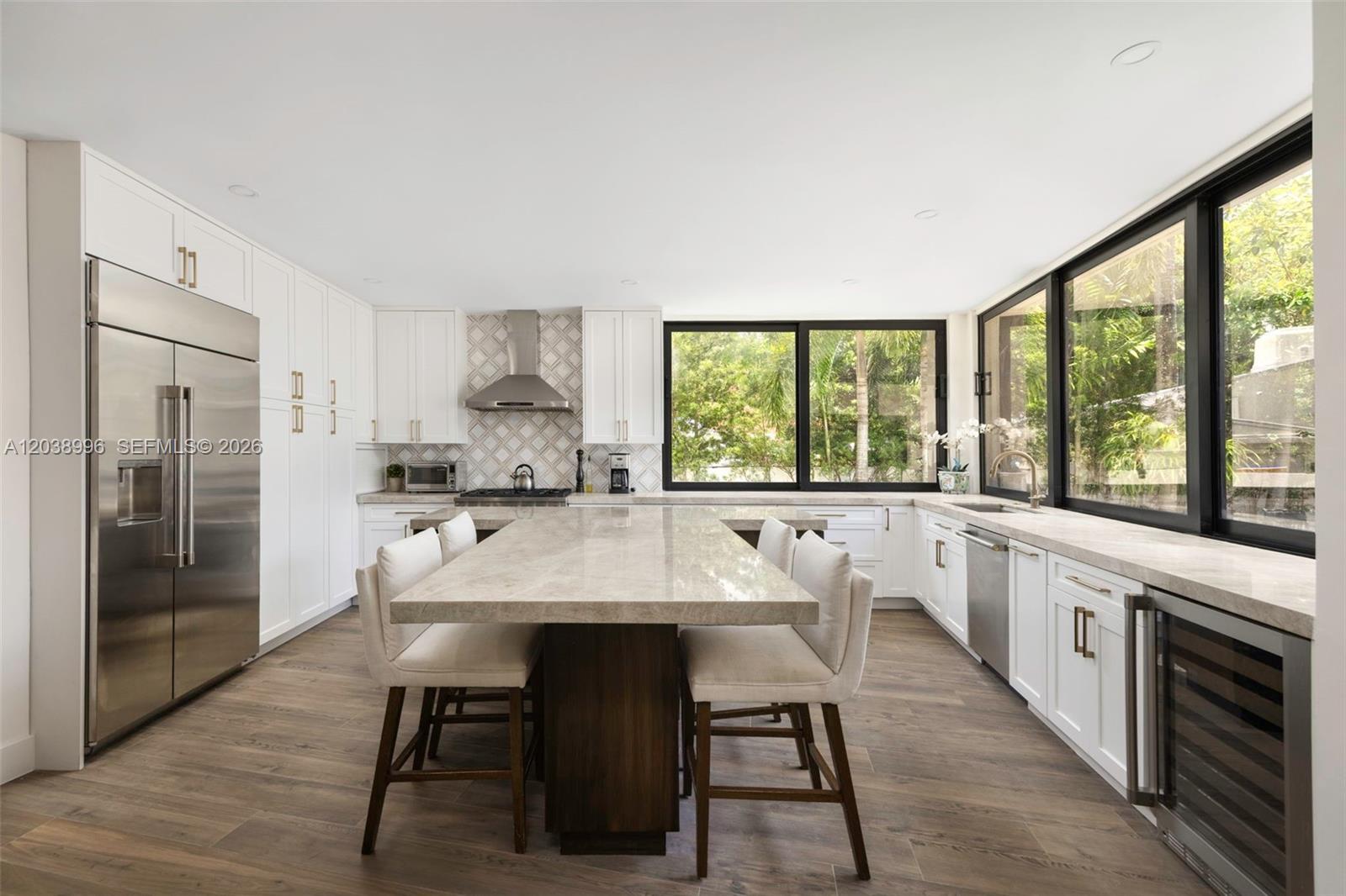 A modern kitchen features white cabinetry, a large stone island, and expansive black-framed windows — 3303 Halissee St, Coconut Grove FL 33133, COCONUT GROVE, FL