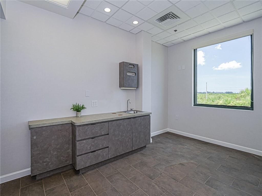 A medical exam room features gray cabinetry, a small sink, tile flooring, and a large window — 3755 7th Terrace, Vero Beach FL 32960, VERO BEACH, FL