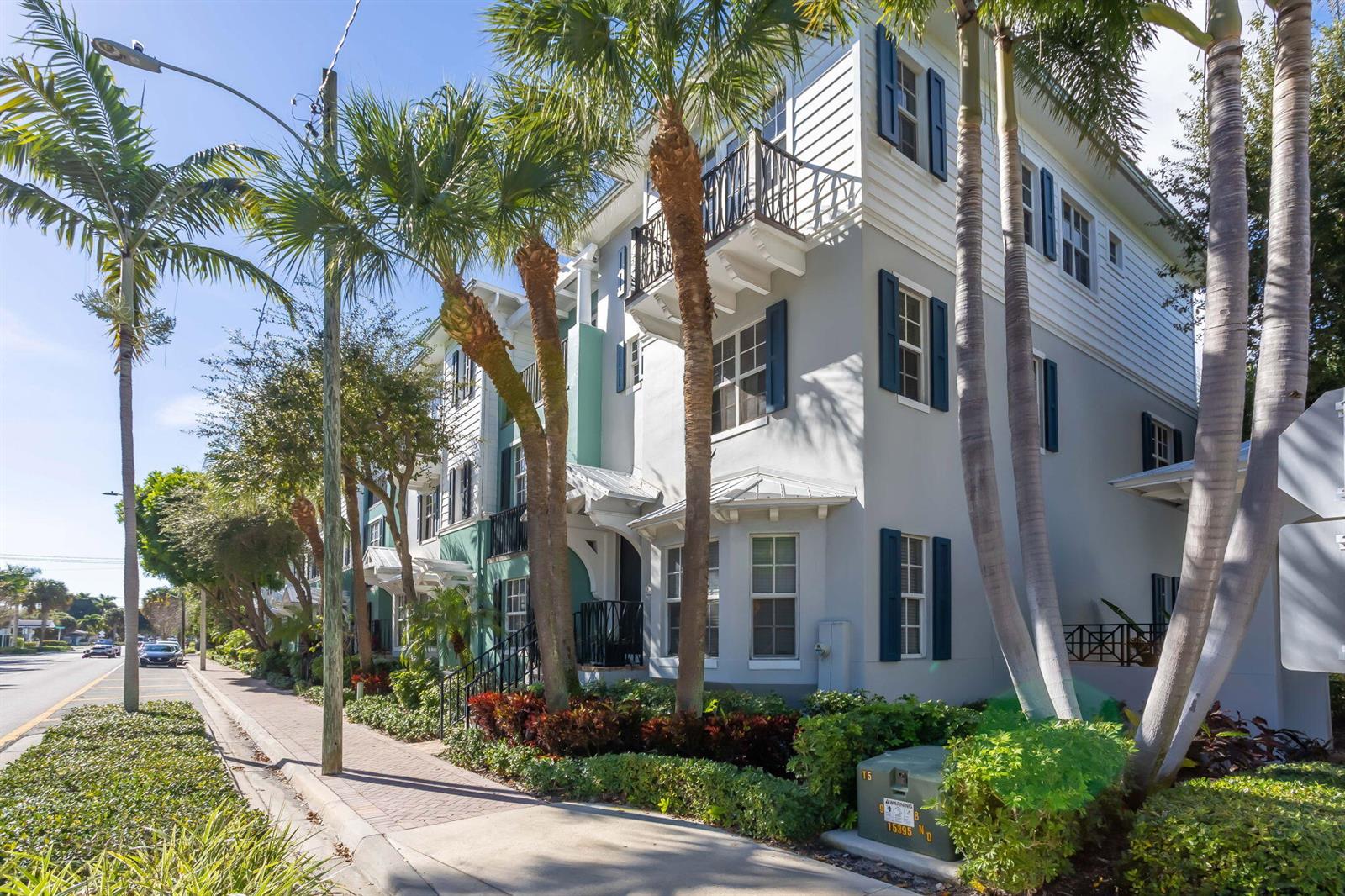 A multi-story building with gray siding, blue shutters, and palm trees along a sidewalk — 349 E Mallory Circle, Delray Beach FL 33483, DELRAY BEACH, FL